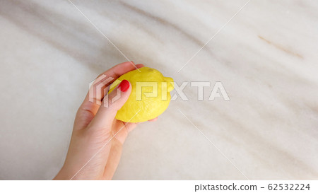 A hand with red nail paint, holding a yellow lemon. A hand with red nail paint, holding a yellow lemon. 62532224