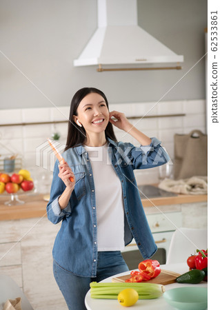Joyful young woman in wireless headphones cooking a salad. Joyful young woman in wireless headphones cooking a salad. 62533861