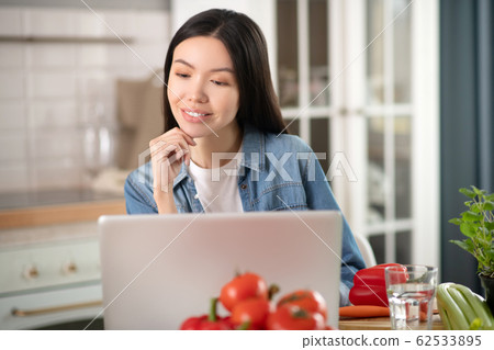 Long-haired young woman busy at laptop at home. 62533895