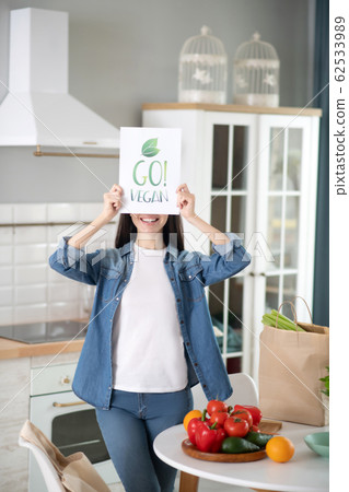 Young woman with a poster in her hands covering her face. 62533989