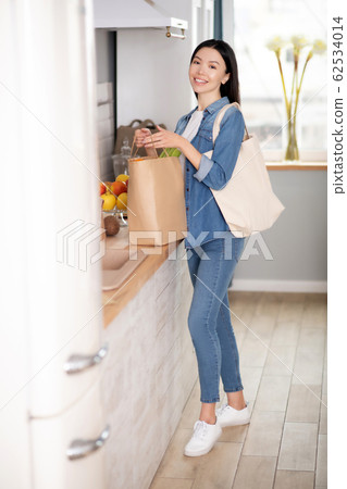 Young woman standing with shopping bags in the kitchen. Young woman standing with shopping bags in the kitchen. 62534014
