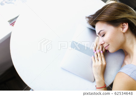 Blonde student lying on laptop at cafe in white background with copy space. 62534648