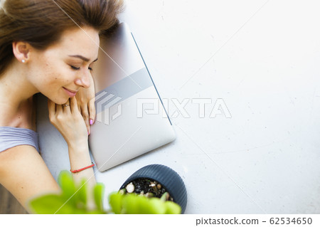 Blonde girl lying on laptop at office in white background with copy space. 62534650