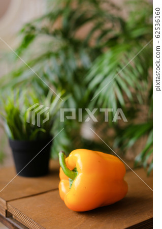 Yellow bellpepper lying on wooden table near houseplants. Yellow bellpepper lying on wooden table near houseplants. 62536160
