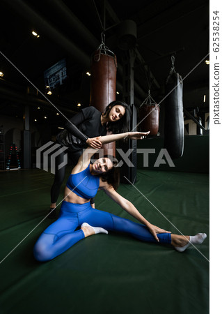 Two beautiful young girls doing fitness in a gym. Stretching the muscles of the legs and arms. Two beautiful young girls doing fitness in a gym. Stretching the muscles of the legs and arms. 62538254