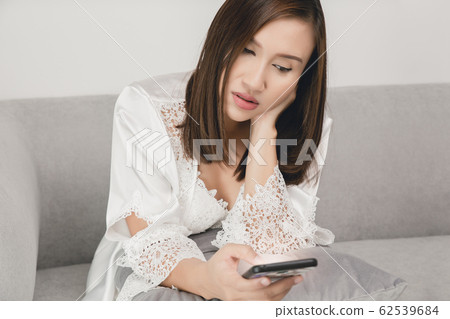 Woman in long sleepwear holding the smartphone, 62539684