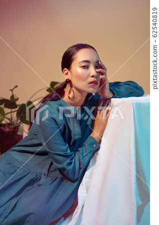 Freestyle. Young woman in long dress with ponytail leaning on cube isolated on neon background touching face tired Freestyle. Young woman in long dress with ponytail leaning on cube isolated on neon background touching face tired 62540819