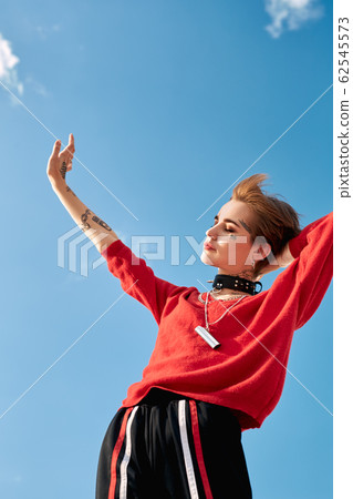 Urban Style. Young stylish woman standing outdoors hand towards sun enjoying freedom smiling happy bottom view Urban Style. Young stylish woman standing outdoors hand towards sun enjoying freedom smiling happy bottom view 62545573