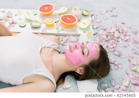 Young healthy woman in spa making treatments and face mask, natural cosmetics and fruits around her. Young woman in a spa with algae facial mask. Young healthy woman in spa making treatments and face mask, natural cosmetics and fruits around her. Young woman in a spa with algae facial mask. 62545605