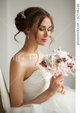 Close up portrait of young bride in a beautiful dress holding a bouquet of flowers in bright white studio. Wedding concept. Close up portrait of young bride in a beautiful dress holding a bouquet of flowers in bright white studio. Wedding concept. 62546286