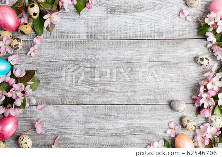 Festive Easter mockup. Frame of pink Apple tree flowers, quail eggs, colored Easter hen eggs on painted grey wooden background. Top view, flat lay, copy space. Festive Easter mockup. Frame of pink Apple tree flowers, quail eggs, colored Easter hen eggs on painted grey wooden background. Top view, flat lay, copy space. 62546706