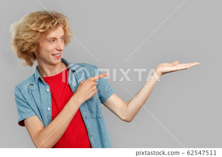 Freestyle. Teen blond boy standing isolated on gray showing copy space smiling playful 62547511