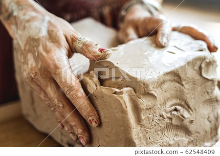 Craftsperson Concept. Young woman making pottery indoors modeling clay hands close-up Craftsperson Concept. Young woman making pottery indoors modeling clay hands close-up 62548409