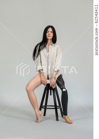 Freestyle. Diverse girl with leg prosthesis sitting on chair isolated on grey full body shot posing smiling joyful Freestyle. Diverse girl with leg prosthesis sitting on chair isolated on grey full body shot posing smiling joyful 62548411