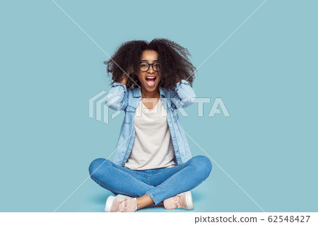 Freestyle. African girl in glasses sitting isolated on gray messing hair shouting excited Freestyle. African girl in glasses sitting isolated on gray messing hair shouting excited 62548427