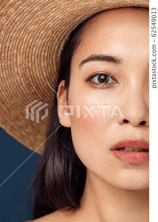 Freestyle. Young woman in hat standing isolated on dark blue half face close-up looking camera curious 62549013