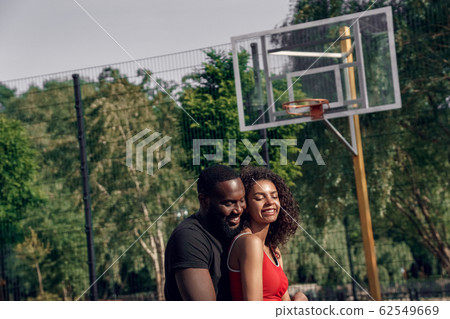 Outdoors Activity. African couple standing on basketball court hugging smiling joyful 62549669