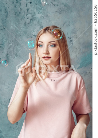 Freestyle. Teen blonde girl in pink clothes standing isolated on grey bursting bubbles pensive Freestyle. Teen blonde girl in pink clothes standing isolated on grey bursting bubbles pensive 62550156