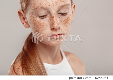 Inclusive Beauty. Girl with freckles standing isolated on grey looking down upset close-up 62550618