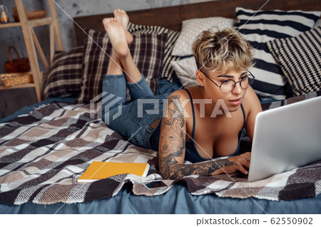 Young adult female lying on bed and working on modern laptop 62550902