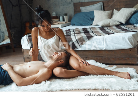Mixed Race Couple. Young man lying on woman laps sitting on floor at home talking joyful Mixed Race Couple. Young man lying on woman laps sitting on floor at home talking joyful 62551201