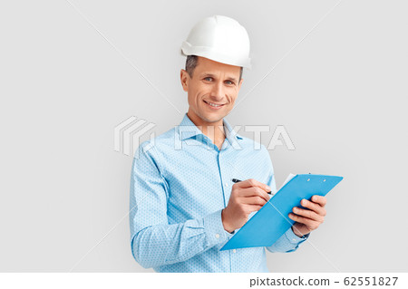Construction. Mature man in hardhat standing isolated on white with clipboard taking notes smiling joyful 62551827