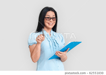 Freestyle. Asian woman in eyeglasses standing isolated on white with clipboard pointing at camera playful Freestyle. Asian woman in eyeglasses standing isolated on white with clipboard pointing at camera playful 62551830