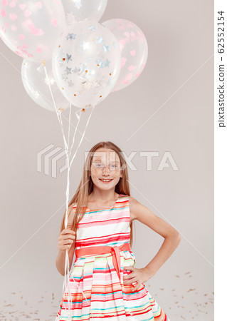 Inclusive Beauty. Girl with freckles in dress standing isolated on grey holding balloons posing smiling cheerful Inclusive Beauty. Girl with freckles in dress standing isolated on grey holding balloons posing smiling cheerful 62552154