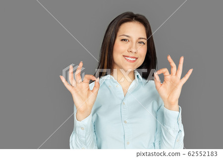 Freestyle. Young woman standing isolated on grey showing ok smiling positive Freestyle. Young woman standing isolated on grey showing ok smiling positive 62552183