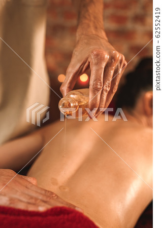 Alternative Medicine. Therapist healing woman doing abhyanga back massage pouring herbal oil on skin close-up 62552419