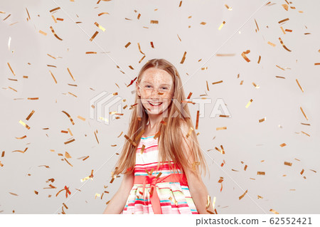 Inclusive Beauty. Girl with freckles standing isolated on grey flying confetti laughig cheerful 62552421