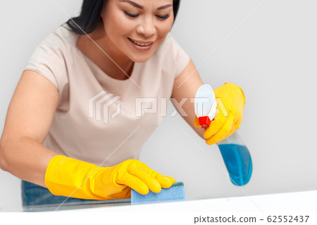 Freestyle. Asian woman in gloves standing isolated on white with spray cleaning surface with sponge smiling concentrated close-up Freestyle. Asian woman in gloves standing isolated on white with spray cleaning surface with sponge smiling concentrated close-up 62552437