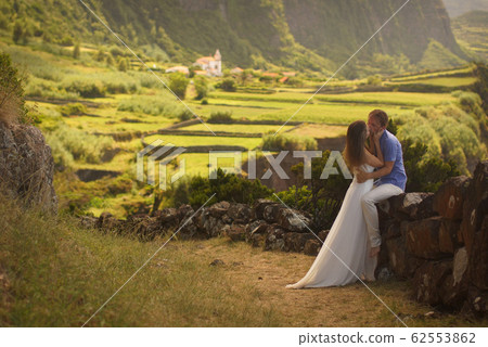 Young newly wedded kissing couple. Attractive woman in white dress hugging man. Romantic background of idyllic landcsape 62553862