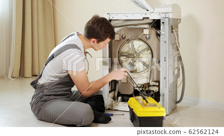 master opens back panel of broken washing machine near wall 62562124