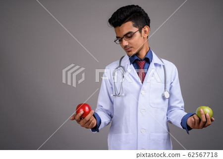 Young Indian man doctor against gray background Young Indian man doctor against gray background 62567718