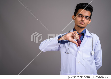 Young Indian man doctor against gray background Young Indian man doctor against gray background 62568227