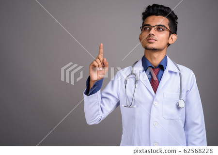 Young Indian man doctor against gray background Young Indian man doctor against gray background 62568228