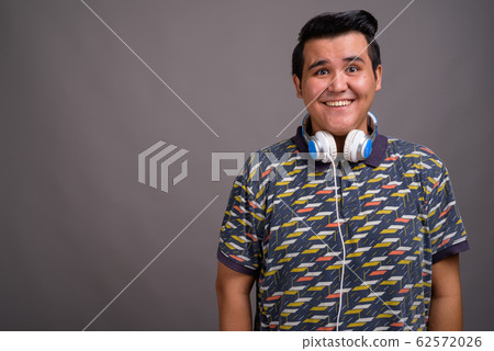 Young multi-ethnic man wearing headphones against gray backgroun Young multi-ethnic man wearing headphones against gray backgroun 62572026