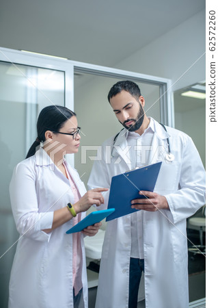 Dark-haired male and female doctors standing in the room together discussing results 62572260