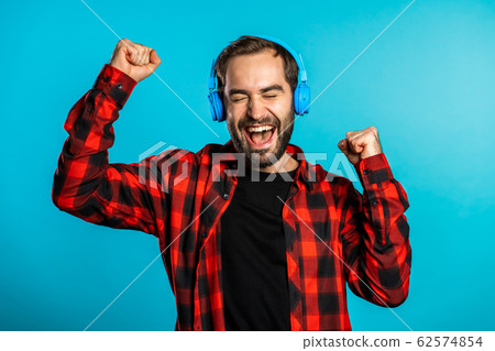 Handsome man with headphones dancing isolated on blue background. Party, music, lifestyle, radio and disco concept. 62574854