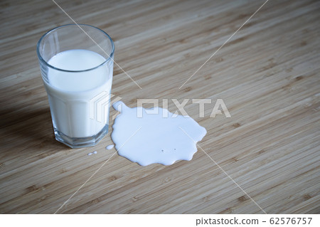 glass on wooden table with milk spilled over in a 62576757