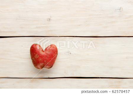 Ugly potato in the heart shape on a white wooden Ugly potato in the heart shape on a white wooden 62578457
