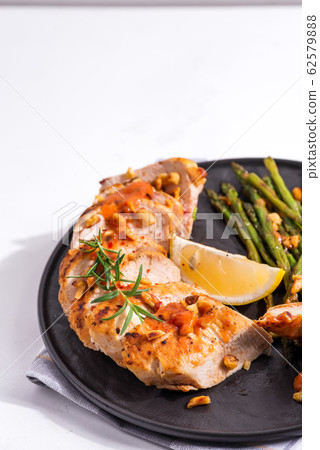 grilled chicken breast fillet with asparagus and lemon in slate plate and white stone background 62579888