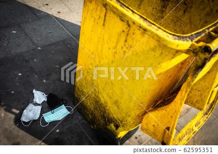 Person littering of garbage of used protective masks throw in the crevices of the bushes,hazardous waste,risk of disease,spread of germ,Coronavirus,Covid 19 virus,concept of throw trash in a trash bin 62595351