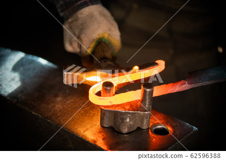 A man blacksmith making a unique handle for the knife - bending the metal A man blacksmith making a unique handle for the knife - bending the metal 62596388