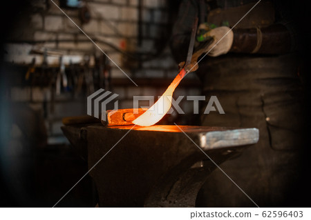 Forging a knife out of the hot metal - holding the knife between the forceps Forging a knife out of the hot metal - holding the knife between the forceps 62596403