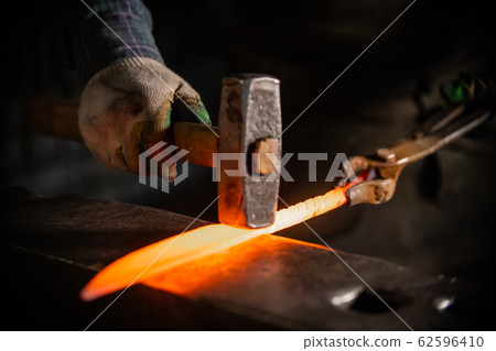 Forging a knife out of the hot metal using a hammer - holding the knife in forceps Forging a knife out of the hot metal using a hammer - holding the knife in forceps 62596410
