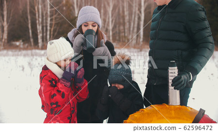 Mother and father with two little kids standing outdoors drinking hot drinks from the thermos Mother and father with two little kids standing outdoors drinking hot drinks from the thermos 62596472