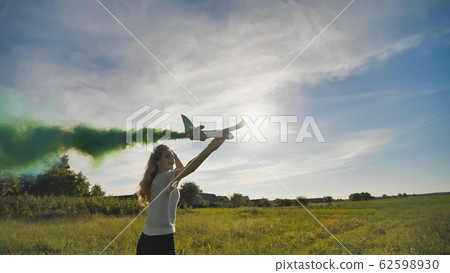 A young girl with a toy airplane smokes colorful smoke on a summer evening. A young girl with a toy airplane smokes colorful smoke on a summer evening. 62598930