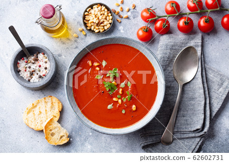 Tomato soup with fresh herbs and pine nuts in a bowl. Grey stone background. Top view. Tomato soup with fresh herbs and pine nuts in a bowl. Grey stone background. Top view. 62602731